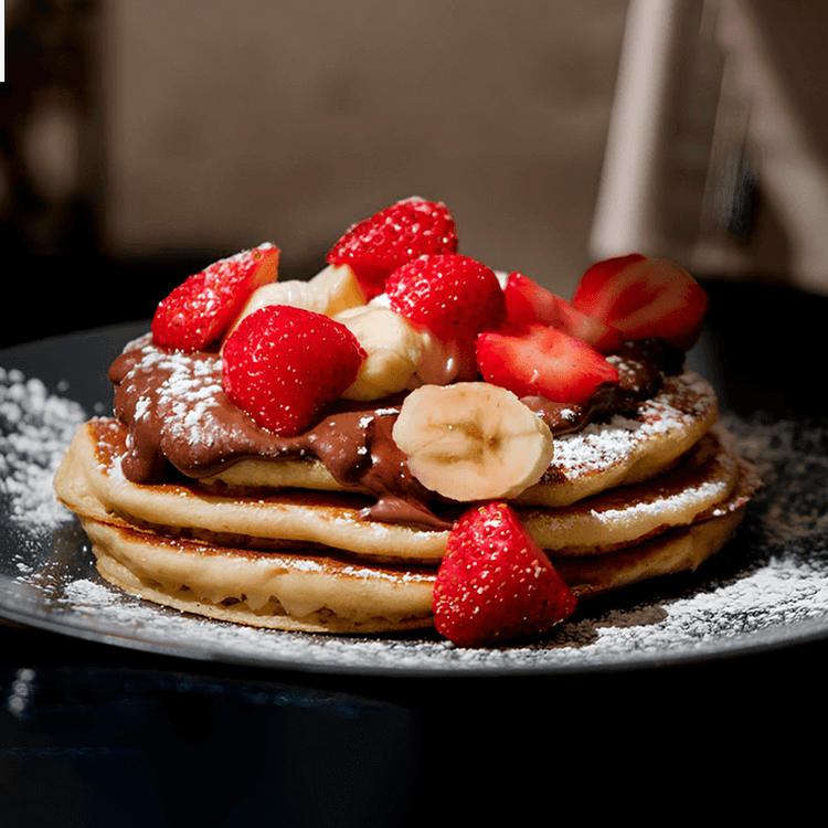 fotografia de pilha de panquecas de banana fit com rodelas de banana e pedaços de morango cobertos por mel e creme de BOLD Whey Milkshake de Baunilha